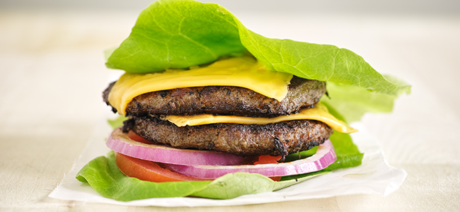 Burger patties with cheese, tomatoes, and red onion wrapped in lettuce.