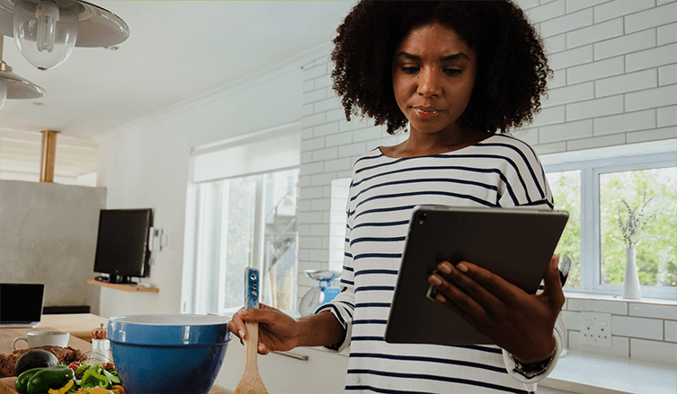  A Black woman with natural hair and a striped shirt reads on a tablet with a  skeptical look on her face while cooking.