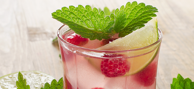 Close-up of a fizzing beverage with floating raspberries, lime, and mint. 