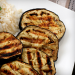 Slices of grilled eggplant on a plate next to rice