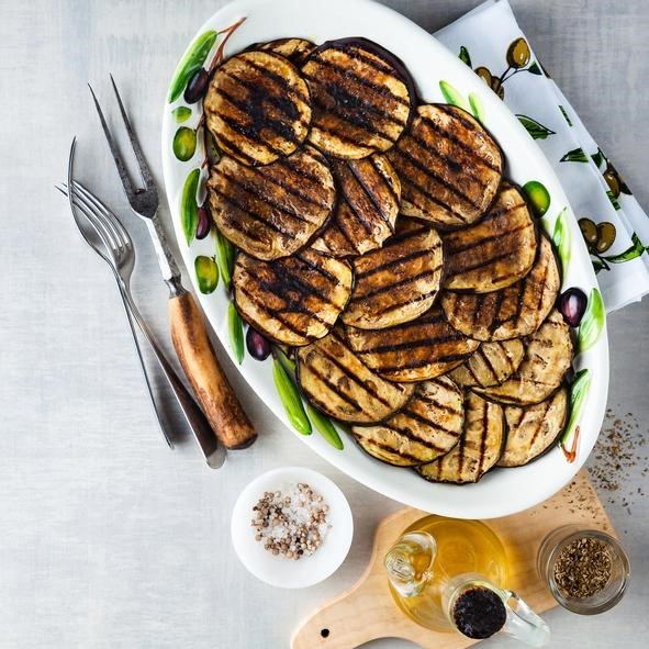 Grilled eggplants seasoned with olive oil on a white stone table