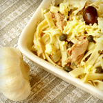 Pasta salad with tuna, capers, and lemon in a dish with a bulb of garlic beside it