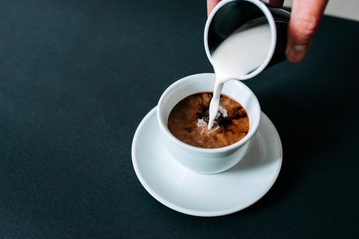 pouring cream into cup of coffee